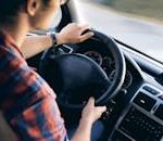 Close-up view of a man driving a modern car, showing dashboard and steering details.