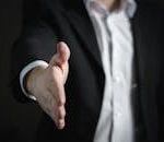 Close-up of a businessman extending hand for a handshake, symbolizing agreement and partnership.
