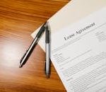 High-angle view of a lease agreement and pens on a wooden desk.